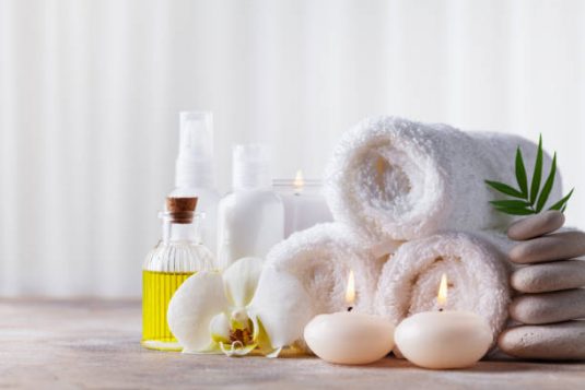 Spa, beauty treatment and wellness background with massage pebbles, orchid flowers, towels, cosmetic products and burning candles. Copy space for text.